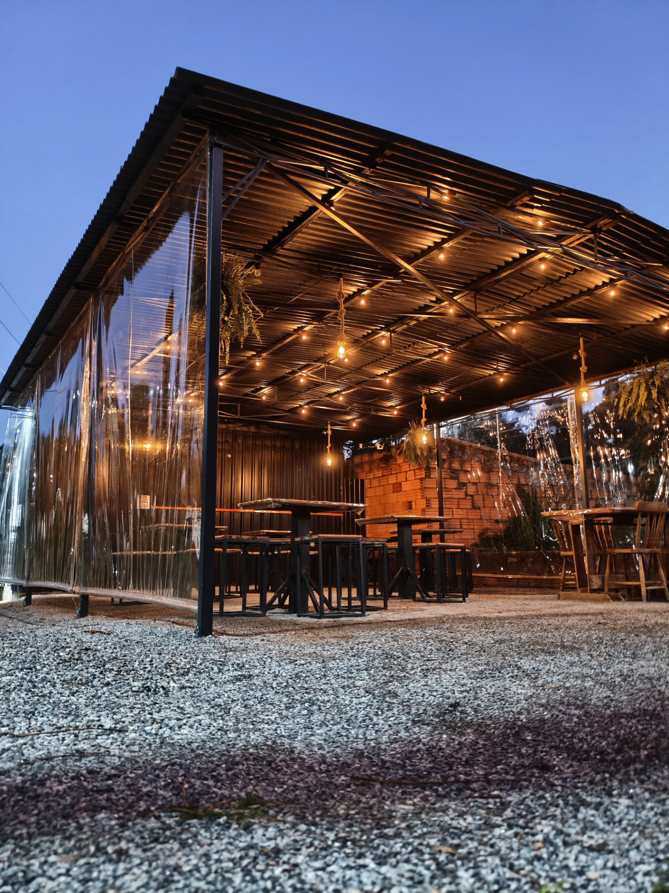 Área externa do Estaleirinho Burger ao entardecer, com iluminação aconchegante e mesas de madeira